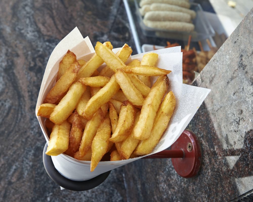 Potatoes fries in a little white paper bag hanging at the wall from a belgian friterie
